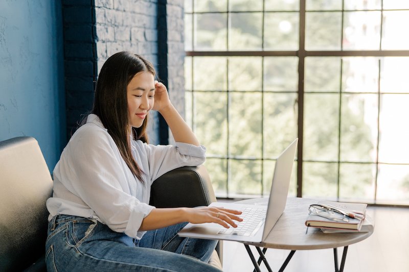 Asian woman sitting on a couch and working on her computer.