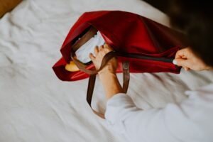 A red bag on a bed with a person's hand reaching in.