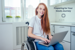 A red headed woman sits smiling in a wheel chair working on her computer.