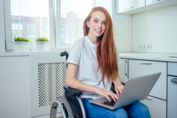 A red headed woman sits in a wheel chair working on her computer as she prepares for her doula journey.