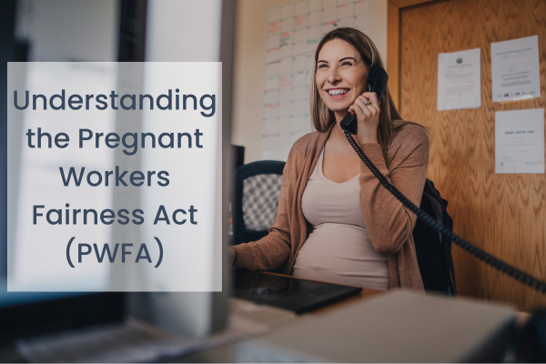 A pregnant woman is smiling while working at a desk and talking on the phone.