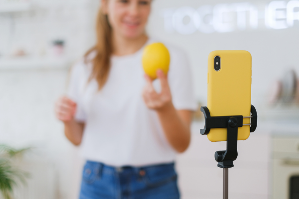 A woman stands in front of a phone filming and instagram reel.