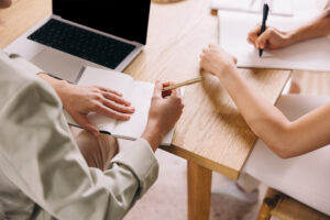 Doulas should think about their contracts. Image: Two sets of hands each working on paperwork at a table.