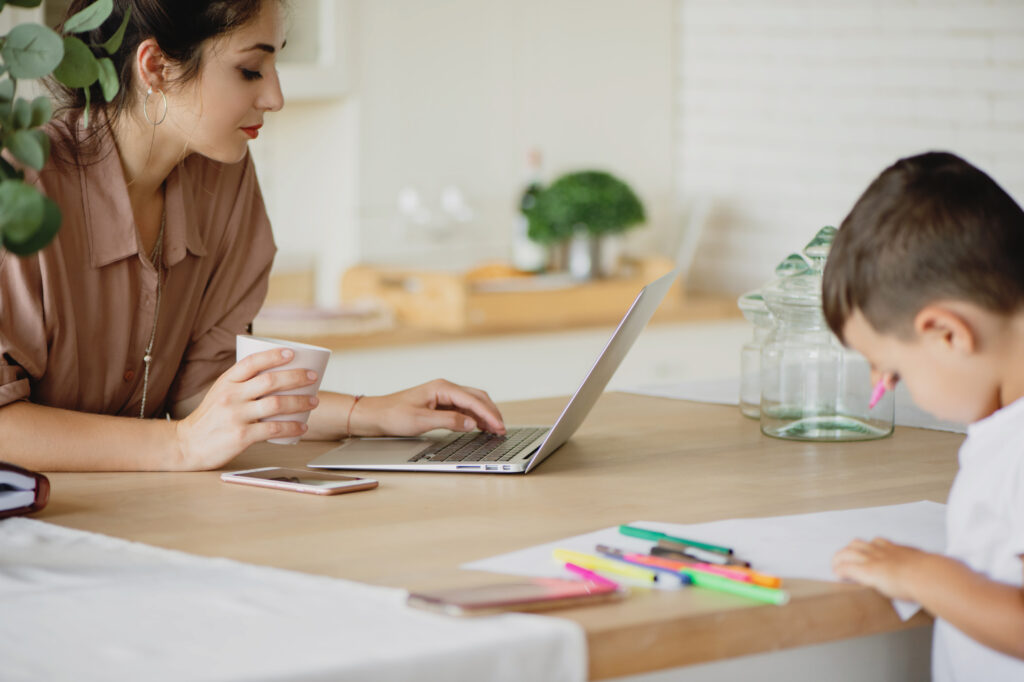 Mom working on her computer while child colors near her.