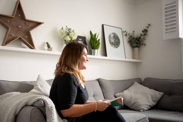 A doula sits on a couch talking to someone off camera with a notebook on her lap.