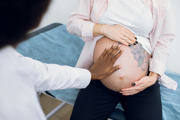 A doula puts her hand on a pregnant abdomen with a visible tattoo.