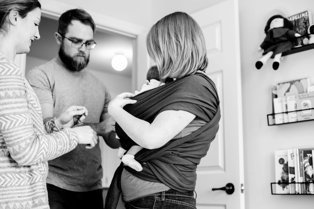 Doula helps a mom and dad learn how to babywear.