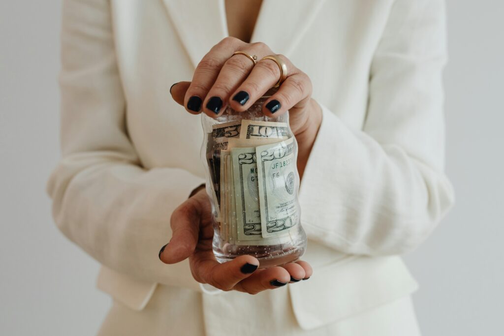 A woman in a white shirt holds up a jar with paper cash in it.