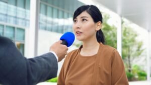 Asian woman in a brown shirt talks to a microphone.