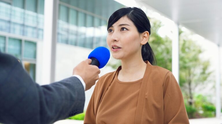 Asian woman in a brown shirt talks to a microphone.
