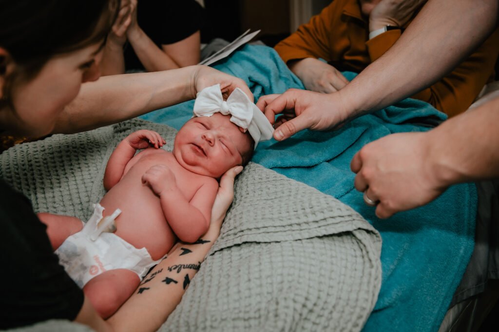 Hands support a newborn wearing a headband.