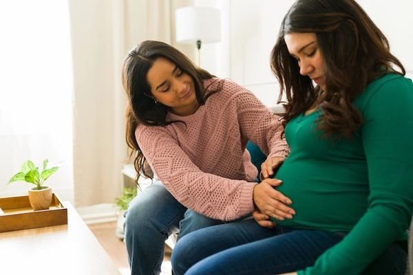 Caring doula supporting expectant mother during prenatal home consultation, offering professional guidance and emotional comfort